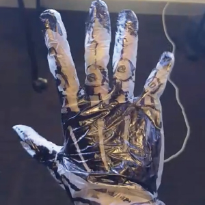A vinyl glove worn on a hand is covered with black marker drawings that outline the bones and joints of the fingers and palm. The glove is part of a low-fidelity prototype used to simulate the robotic hand.